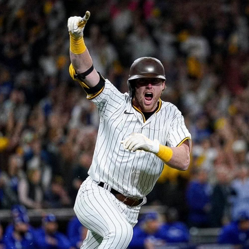 Baseball player in white pinstripe uniform celebrating with fist raised while running on a field with cheering crowd