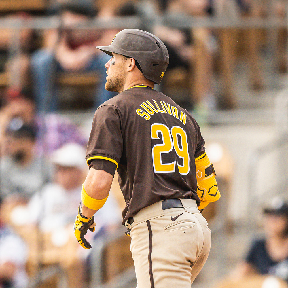 Baseball player running on the field wearing a brown and yellow uniform and helmet with number 29, blurred stadium crowd behind